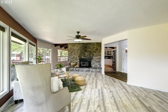 living room with a wood stove, wood finished floors, ceiling fan, and baseboards