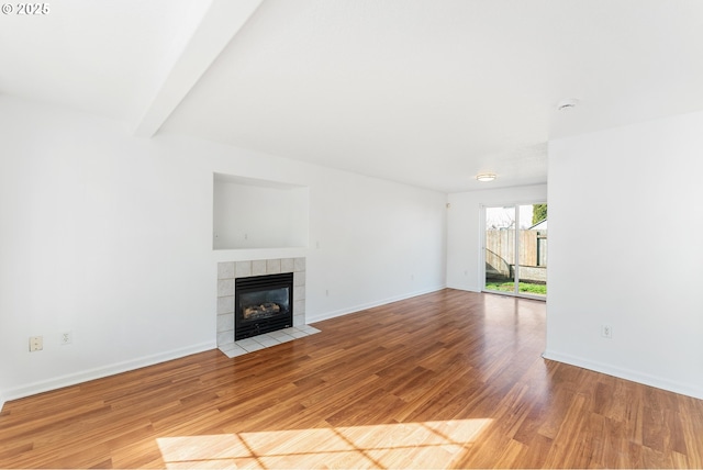 unfurnished living room featuring a tile fireplace, beamed ceiling, baseboards, and wood finished floors