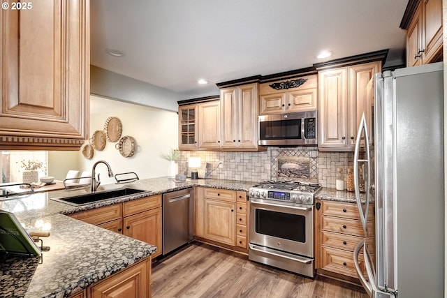 kitchen with sink, stone counters, hardwood / wood-style flooring, stainless steel appliances, and backsplash