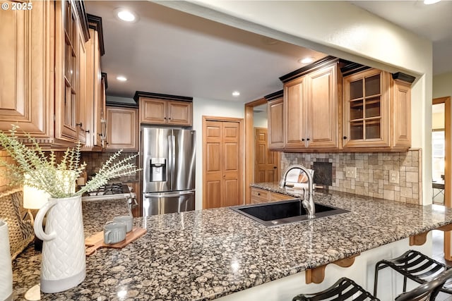 kitchen with stainless steel refrigerator with ice dispenser, a kitchen bar, sink, dark stone counters, and backsplash