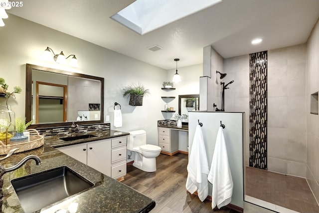 bathroom featuring hardwood / wood-style floors, a skylight, vanity, tiled shower, and toilet