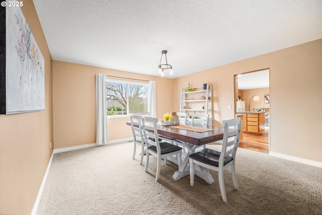 dining space with baseboards, a textured ceiling, and light colored carpet