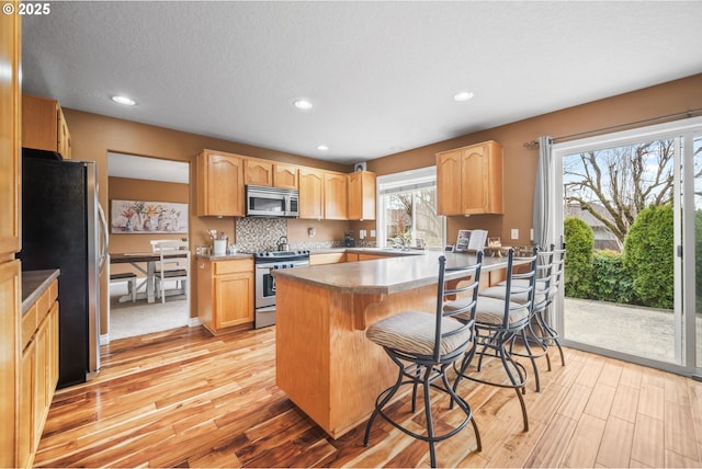 kitchen featuring a breakfast bar area, light brown cabinets, a peninsula, appliances with stainless steel finishes, and light wood finished floors