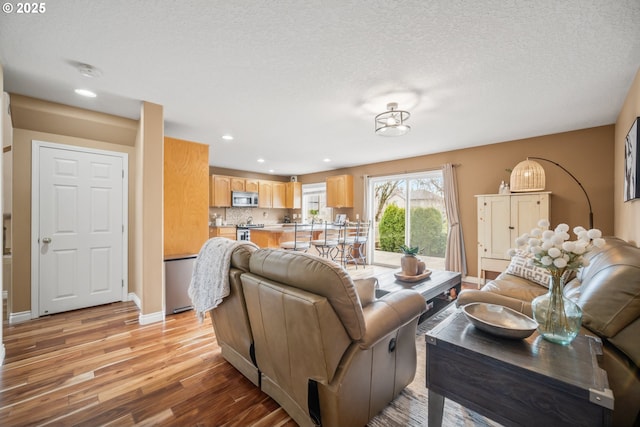 living area with a textured ceiling, recessed lighting, light wood-type flooring, and baseboards