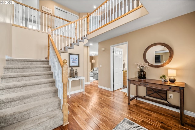 stairway featuring a towering ceiling, baseboards, and wood finished floors