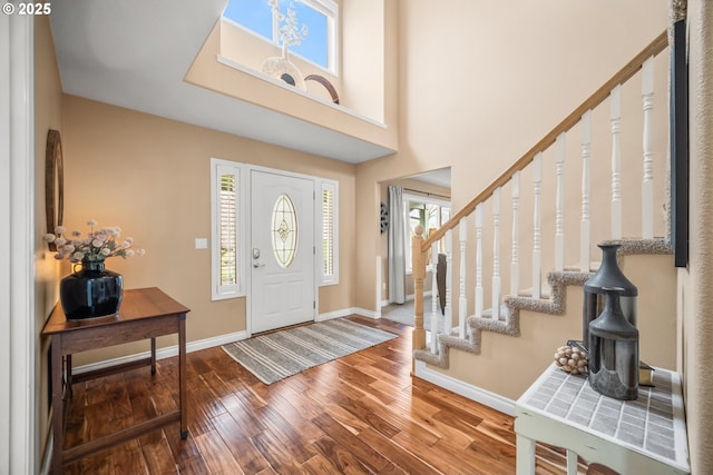 entryway with a towering ceiling, baseboards, stairway, and wood finished floors