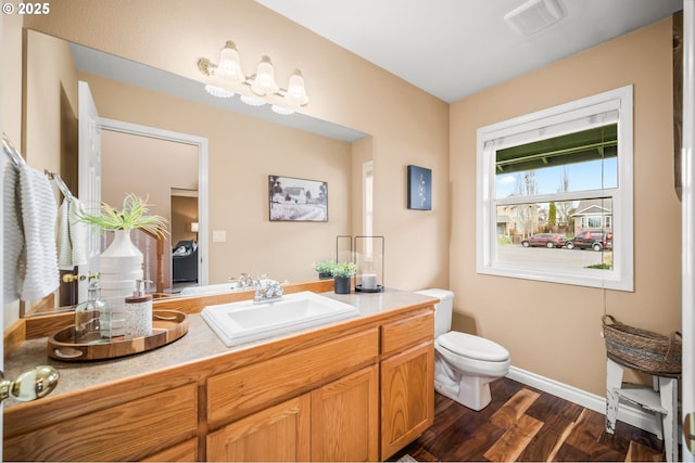 bathroom with visible vents, toilet, vanity, wood finished floors, and baseboards