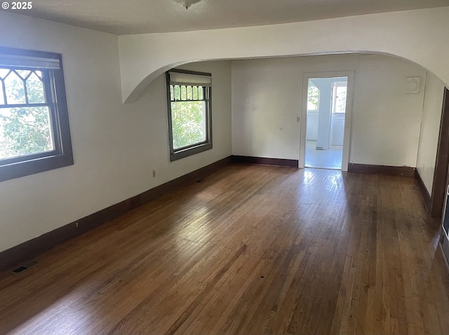 spare room with arched walkways, healthy amount of natural light, and dark wood-style flooring