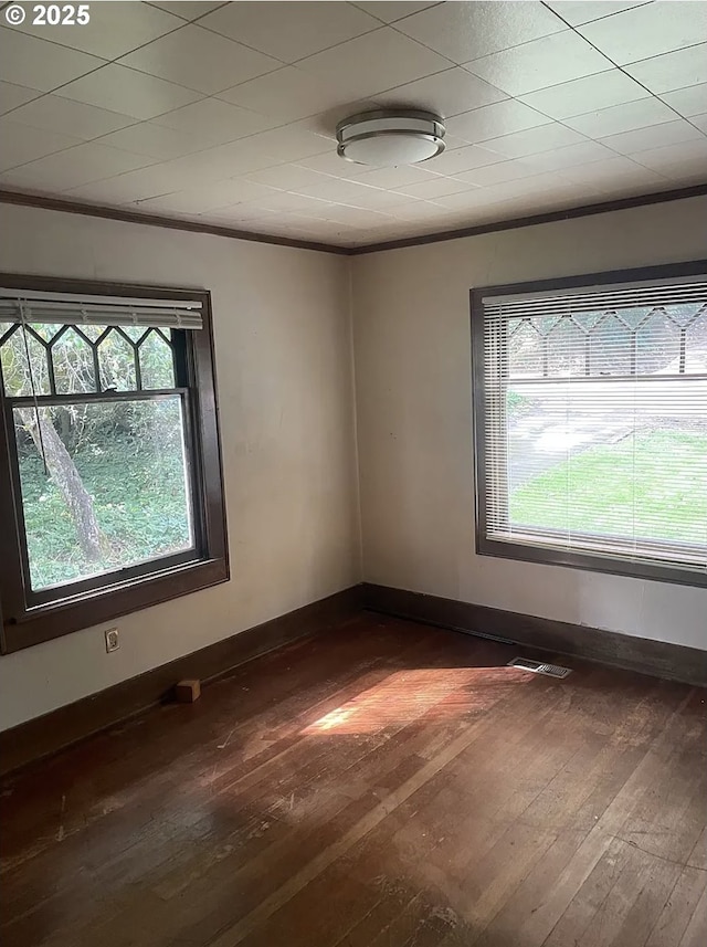 spare room featuring dark wood finished floors, crown molding, and baseboards