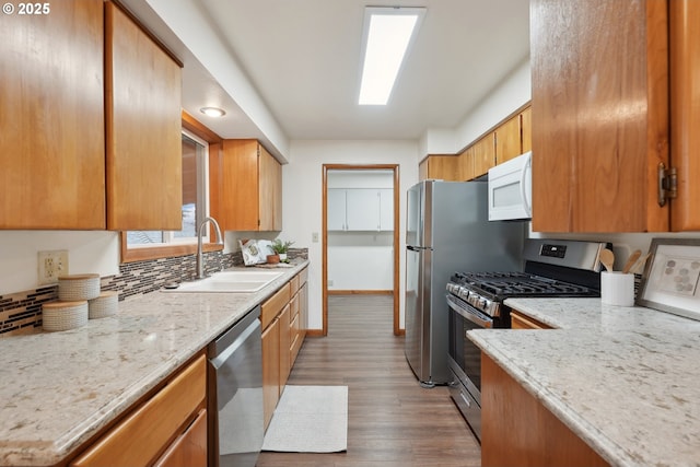 kitchen with appliances with stainless steel finishes, sink, light stone counters, light hardwood / wood-style floors, and decorative backsplash