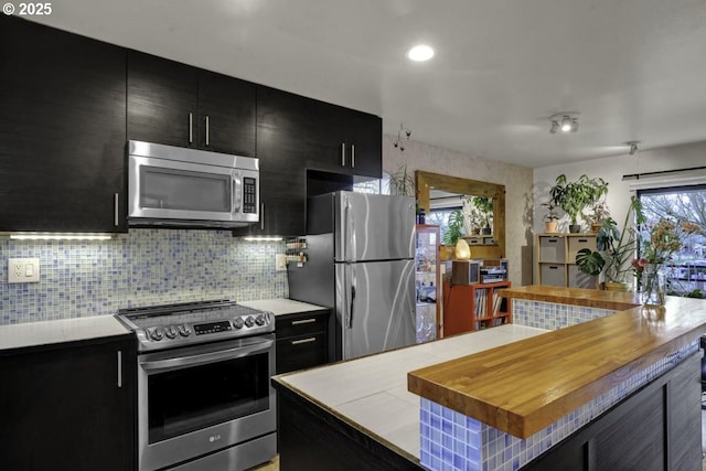 kitchen with butcher block counters, a center island, dark cabinetry, appliances with stainless steel finishes, and backsplash