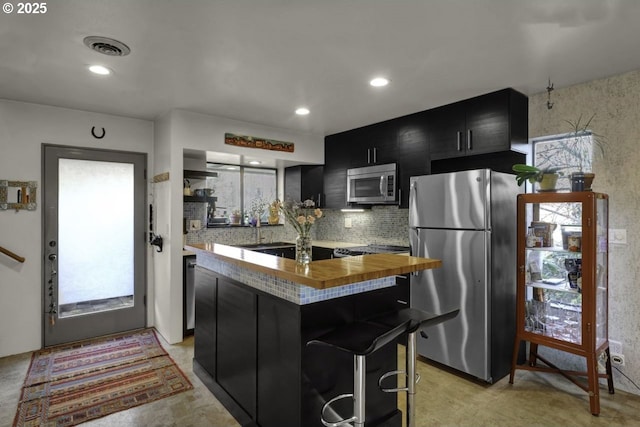kitchen featuring visible vents, butcher block counters, a center island, dark cabinets, and appliances with stainless steel finishes