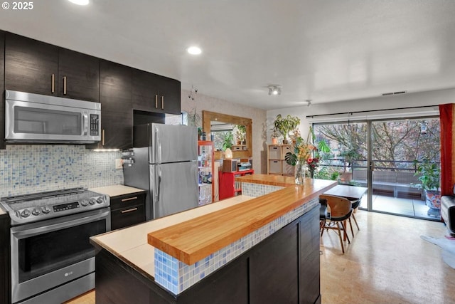 kitchen featuring appliances with stainless steel finishes, dark cabinets, a center island, recessed lighting, and backsplash