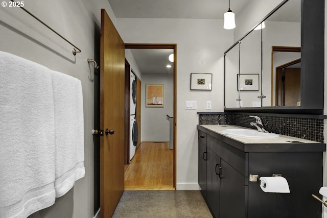 bathroom with baseboards, stacked washing maching and dryer, decorative backsplash, and vanity