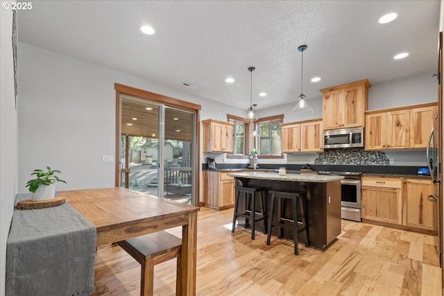 kitchen with light wood-style flooring, stainless steel appliances, a breakfast bar, a kitchen island, and light brown cabinetry