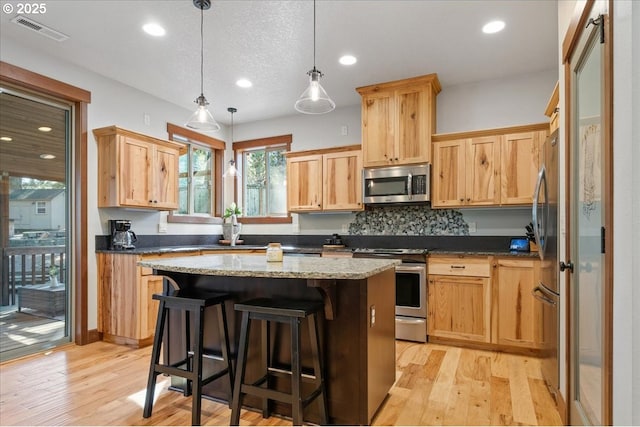 kitchen featuring a center island, stainless steel appliances, visible vents, light wood-style floors, and a kitchen bar