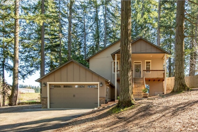 view of front facade featuring dirt driveway, covered porch, stairway, an attached garage, and fence