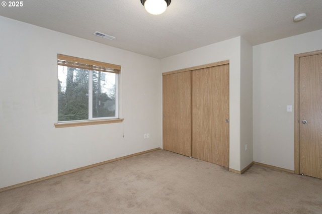 unfurnished bedroom featuring a textured ceiling, light carpet, visible vents, baseboards, and a closet