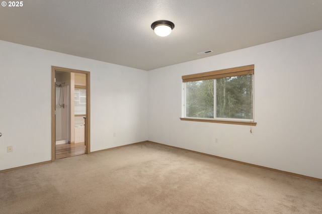 carpeted empty room with visible vents, a textured ceiling, and baseboards