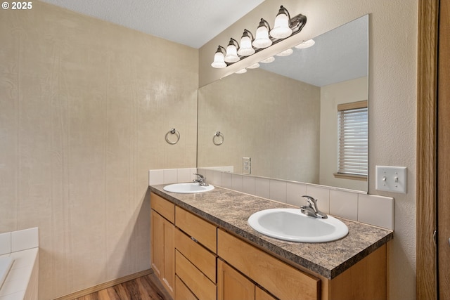 full bathroom with a textured ceiling, double vanity, wood finished floors, and a sink