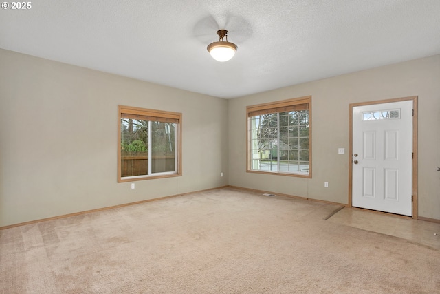 foyer featuring a textured ceiling, baseboards, and light colored carpet