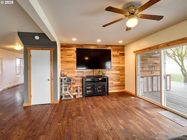 unfurnished living room featuring ceiling fan, wood walls, a textured ceiling, wood finished floors, and baseboards