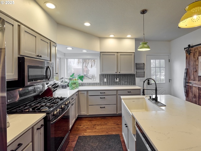 kitchen with a barn door, dark wood-style flooring, stainless steel appliances, pendant lighting, and a sink