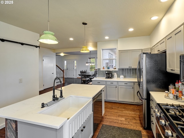 kitchen featuring stainless steel gas stove, dark wood finished floors, dishwashing machine, a kitchen island with sink, and a sink