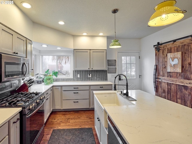 kitchen with dark wood-style flooring, decorative light fixtures, stainless steel appliances, a barn door, and a sink