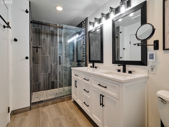 bathroom with a stall shower, a sink, toilet, and double vanity