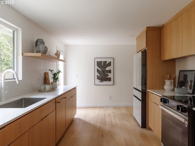 kitchen featuring open shelves, decorative backsplash, freestanding refrigerator, light wood-style floors, and a sink