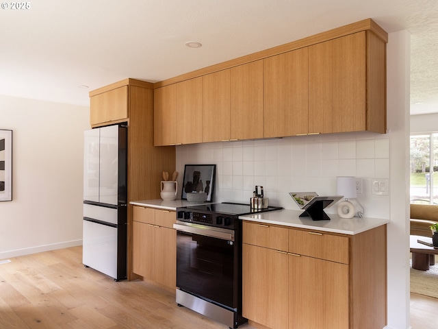 kitchen with freestanding refrigerator, decorative backsplash, light wood-type flooring, light countertops, and electric range oven