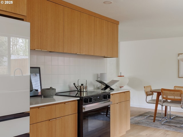 kitchen with light countertops, light wood-style flooring, electric stove, baseboards, and decorative backsplash