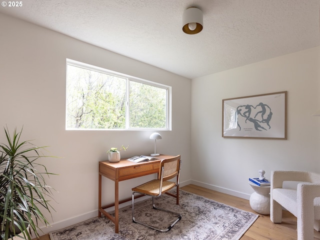 office area with baseboards, a textured ceiling, and light wood finished floors