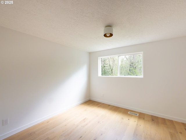 spare room featuring visible vents, a textured ceiling, baseboards, and light wood-style floors