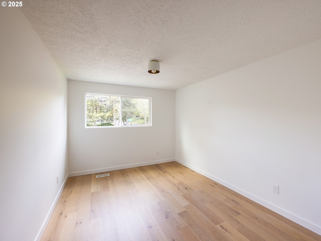 empty room with a textured ceiling, baseboards, visible vents, and light wood-style floors