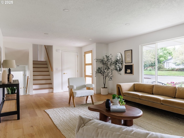 living room with stairway, baseboards, light wood-style flooring, and a textured ceiling
