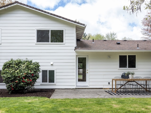 rear view of house with a lawn, a shingled roof, and a patio area