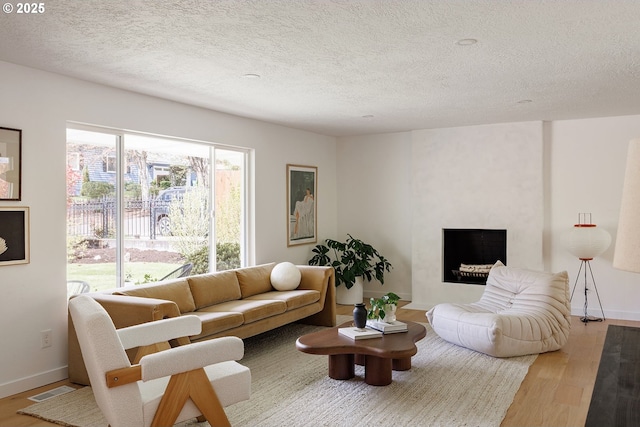 living room featuring a textured ceiling, baseboards, wood finished floors, and visible vents