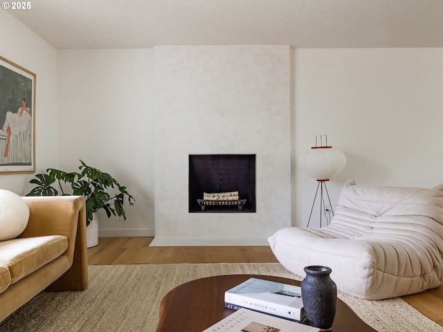 living area featuring baseboards, a fireplace with flush hearth, and wood finished floors