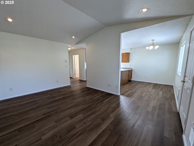 unfurnished living room featuring baseboards, lofted ceiling, dark wood finished floors, and a notable chandelier