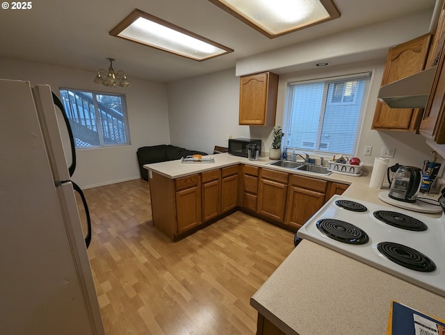 kitchen featuring black microwave, a sink, light wood-style floors, freestanding refrigerator, and a peninsula