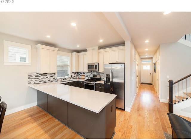 kitchen with stainless steel appliances, light countertops, backsplash, a sink, and a peninsula