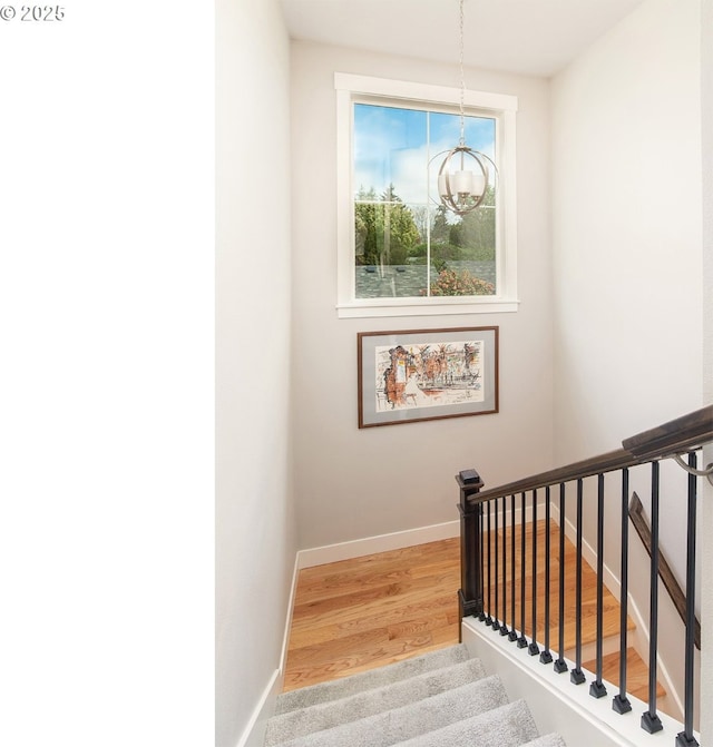 staircase with baseboards, wood finished floors, and a notable chandelier