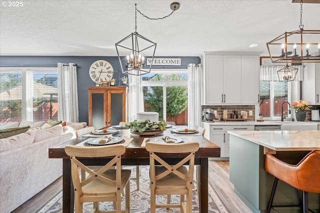 dining space with an inviting chandelier, a wealth of natural light, a textured ceiling, and light wood-type flooring