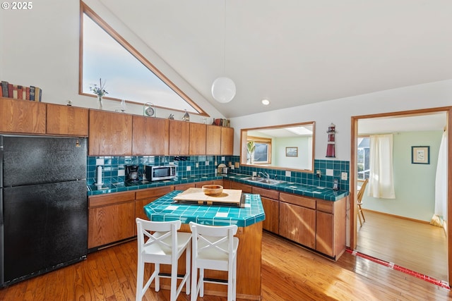 kitchen with tile countertops, brown cabinets, freestanding refrigerator, decorative backsplash, and stainless steel microwave