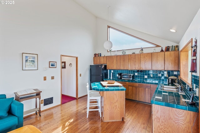 kitchen featuring tile counters, brown cabinetry, a kitchen island, freestanding refrigerator, and a sink