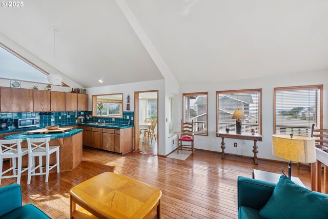 kitchen featuring brown cabinets, lofted ceiling, stainless steel microwave, and tasteful backsplash