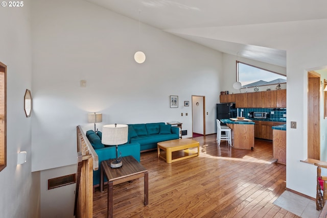 living room featuring baseboards, high vaulted ceiling, and light wood-style floors