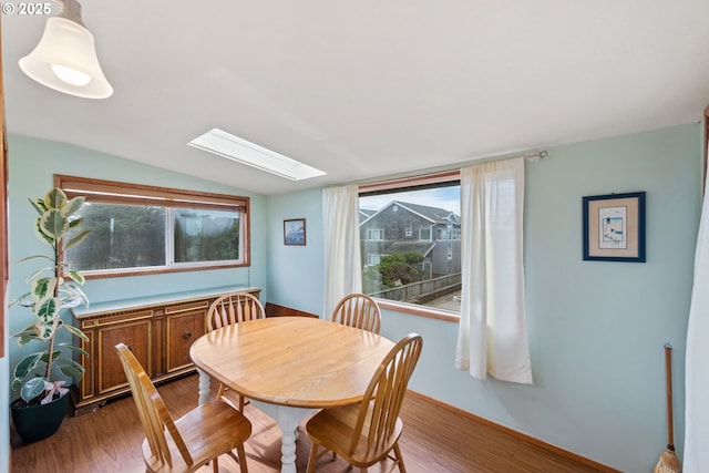 dining area with a healthy amount of sunlight, vaulted ceiling with skylight, and wood finished floors